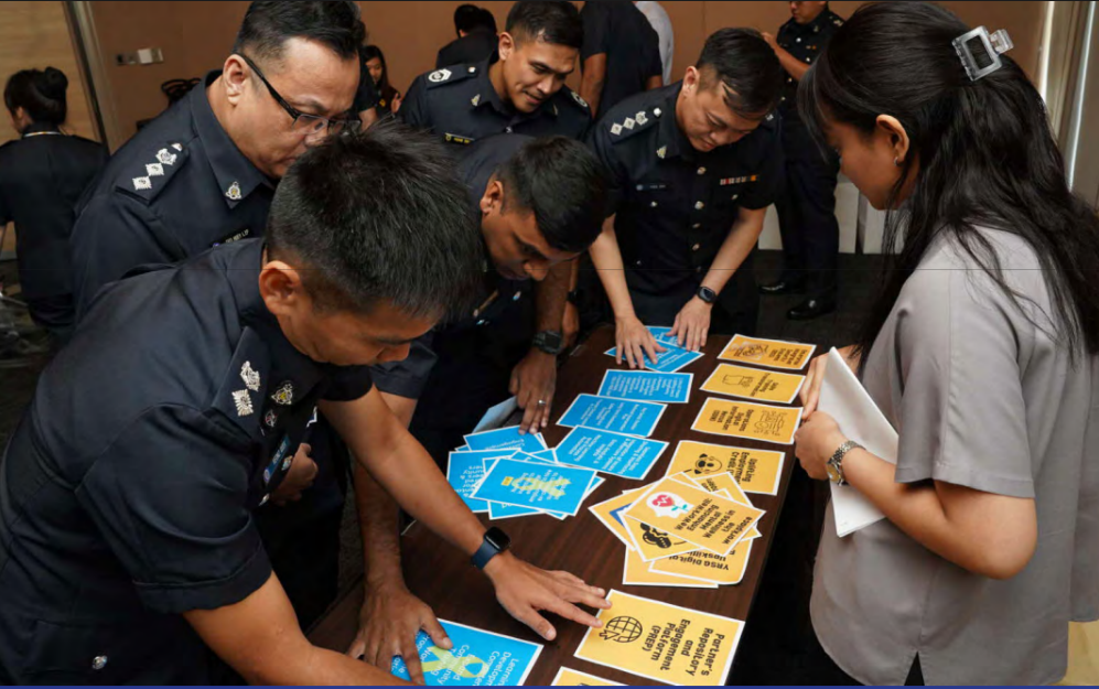 Uniformed officers and a woman gather around a table arranging blue and orange informational cards.